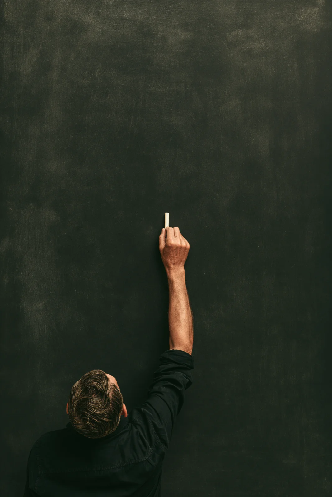 A tutor reaching up to write on a large, almost empty blackboard